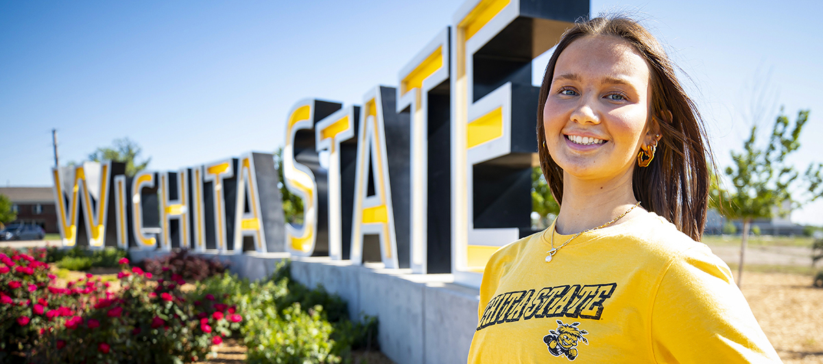 Student posing for a photo in front of the Wichita State sign.