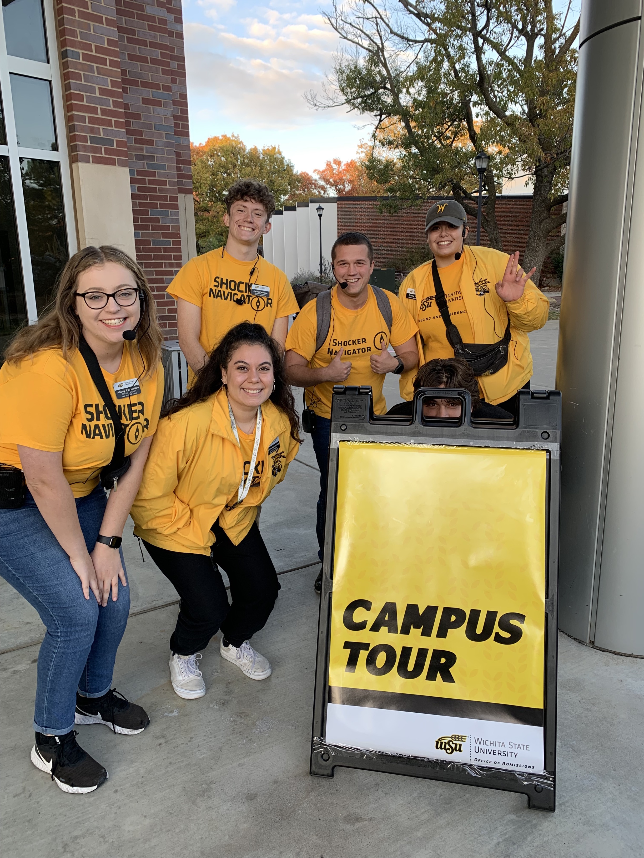 Group of tour guides huddled at a campus visit sign